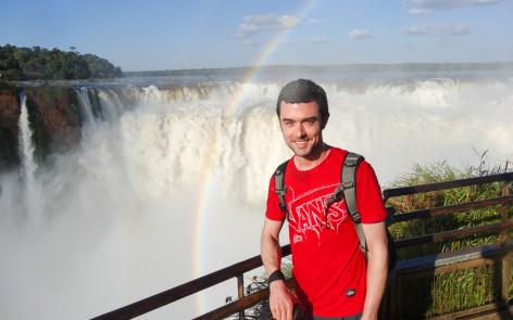 Man overlooking Iguazu Falls with rainbow